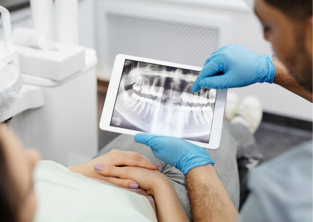 Dentist reviewing a panoramic X-ray with a patient to evaluate bone health and explain who does dental implants.