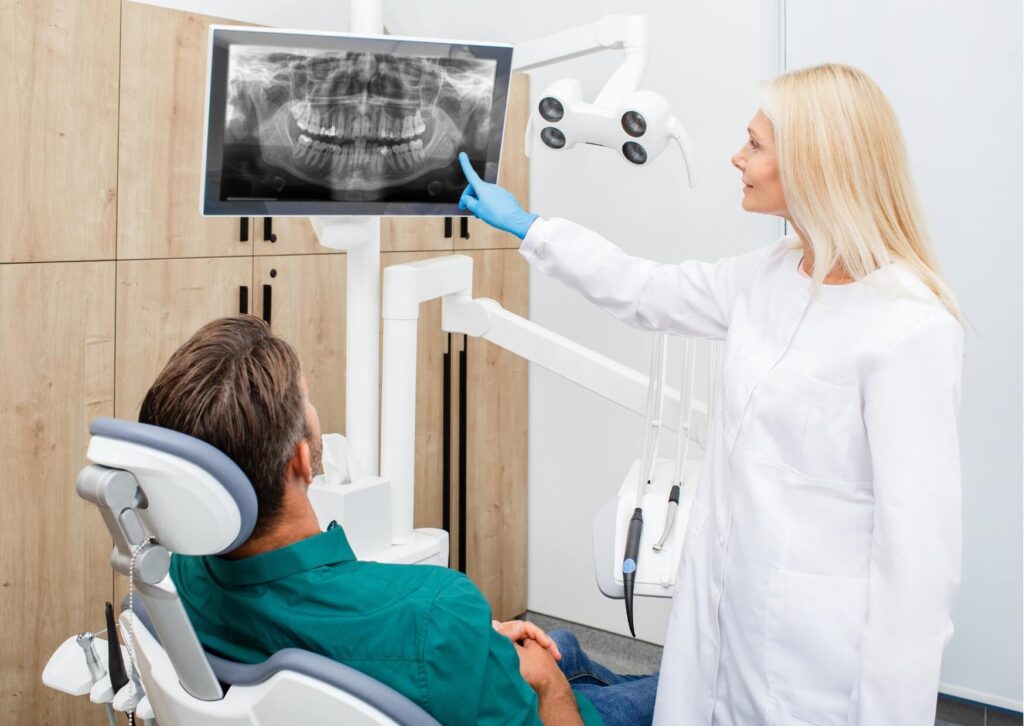Dentist reviewing a panoramic dental X-ray with a patient to evaluate wisdom tooth development and estimate how long a wisdom tooth takes to come in once it starts.