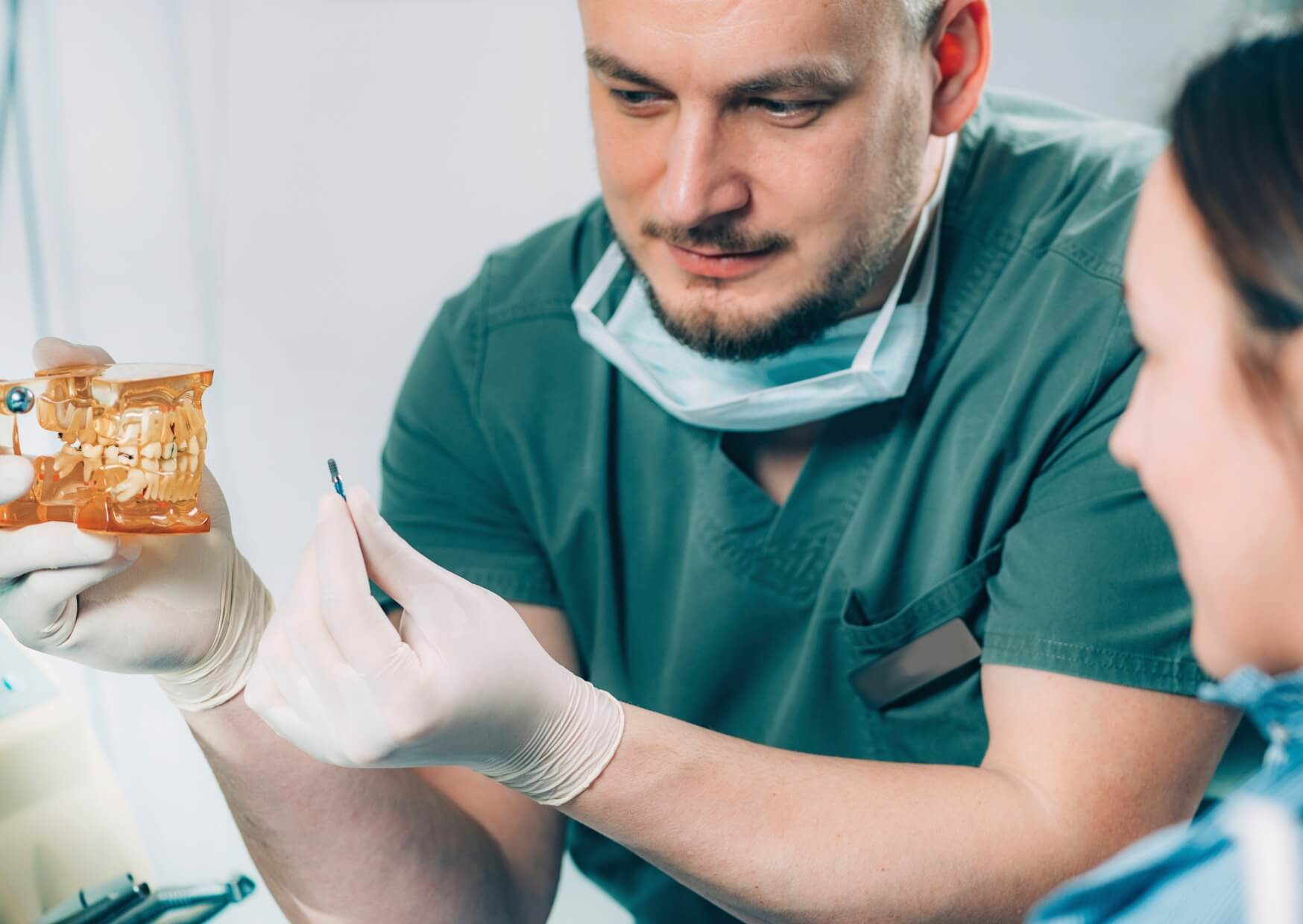 Dental implant specialist explaining the implant procedure with a jaw model during a consultation about who does dental implants.