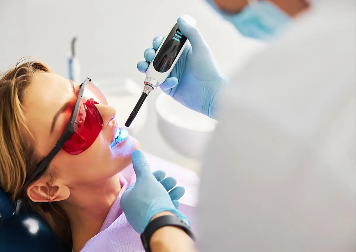 Dentist using a curing light to harden dental sealants applied to a patient’s teeth.