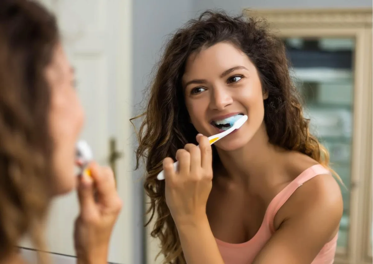 Woman brushing her teeth as part of an oral care routine alongside salt water rinses for gum healing.