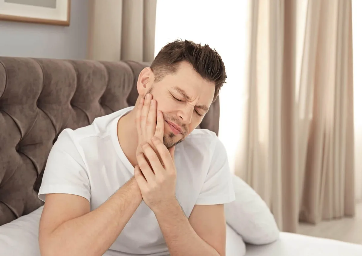Man holding his cheek in pain from a possible cavity, highlighting symptoms of tooth decay that can develop over time.