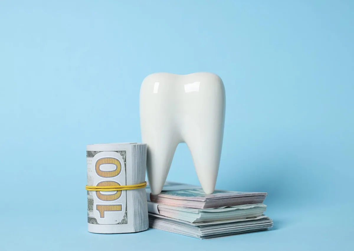 Tooth model beside stacks of cash, illustrating teeth bonding costs and factors that affect treatment pricing.